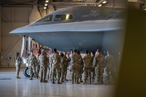 Approximately 20 U.S. Army and Air Force troops gather in an aircraft hangar around a B-2 Spirit stealth bomber. The troops are wearing OCP pattern uniforms.