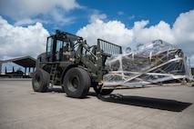 A service member drives a forklift loaded with cargo.