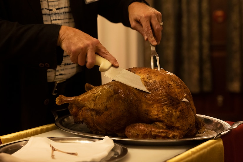 A person is carving a baked turkey with a large knife.
