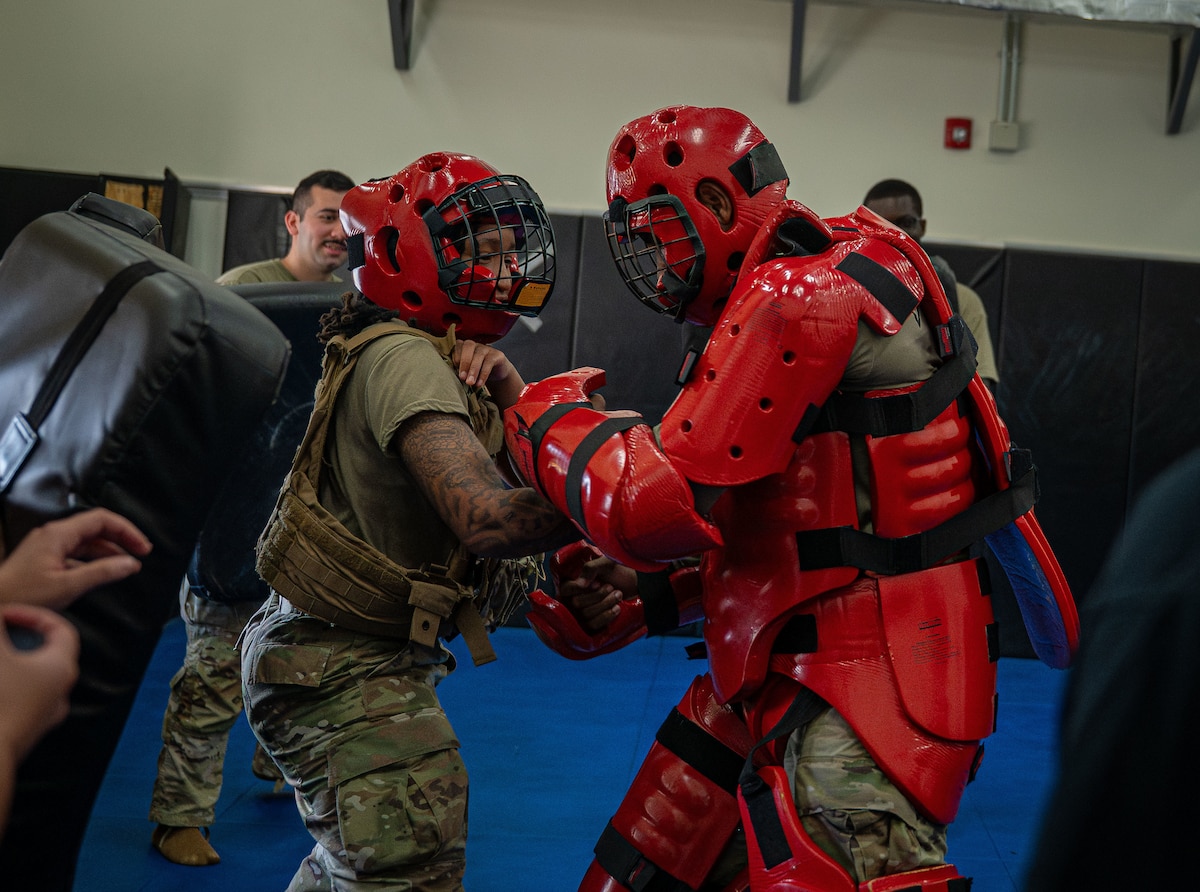 A group of Airmen simulate fighting in a red suit.