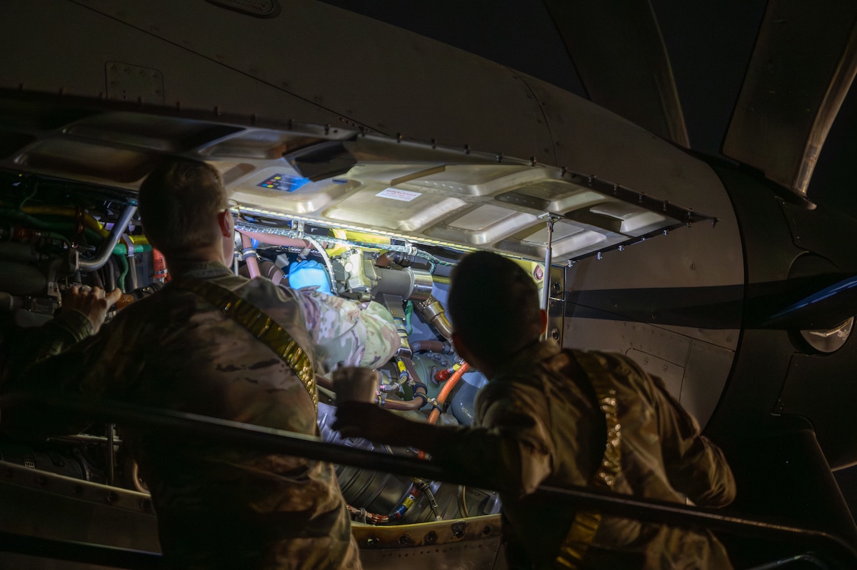Two military members use a flashlight to inspect the inside panel of a C-130J aircraft.