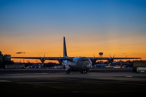 A C-130J sits on the flightline as the sun rises.