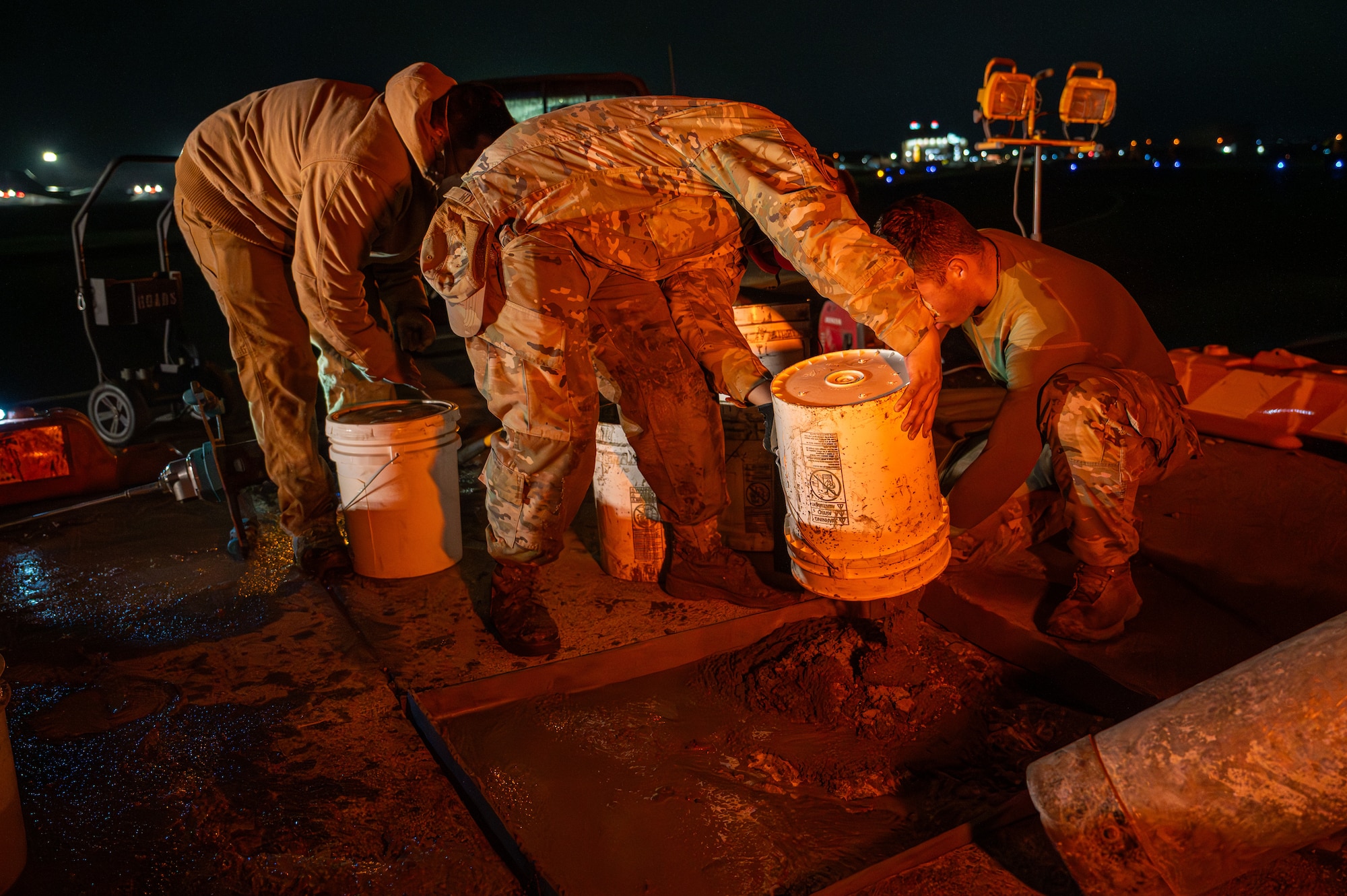 Three Airmen pour concrete into a space on the ground.