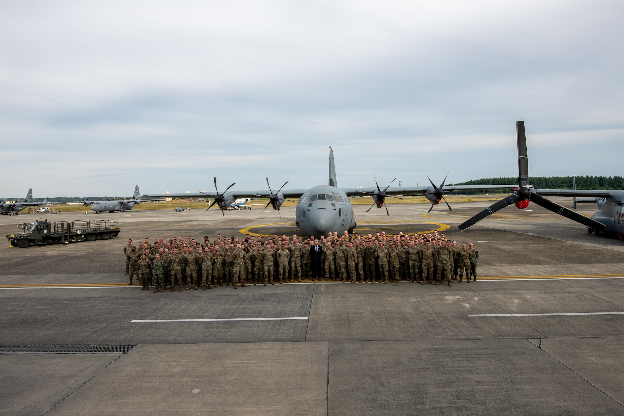 U.S. service members and the U.S. Secretary of War pose for a photo in font of static displays on the flightline.
