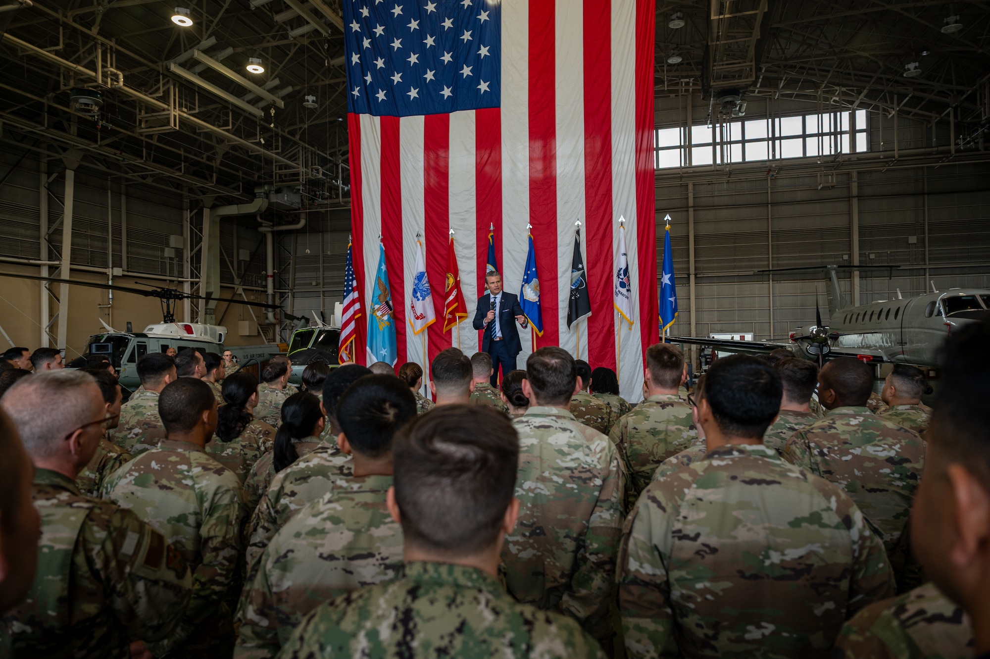 U.S. Secretary of War Pete Hegseth speaks to U.S. service members on stage in front of an American flag.