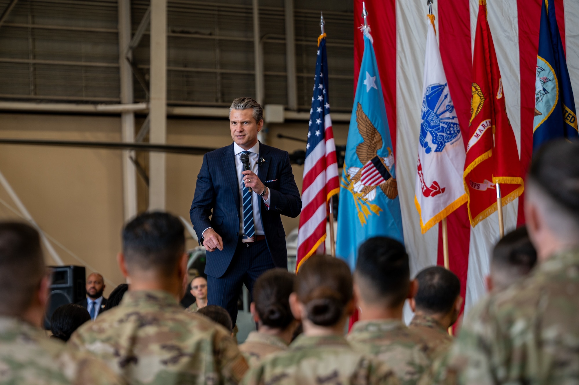 U.S. Secretary of War Pete Hegseth speaks to U.S. service members on stage in front of an American flag.