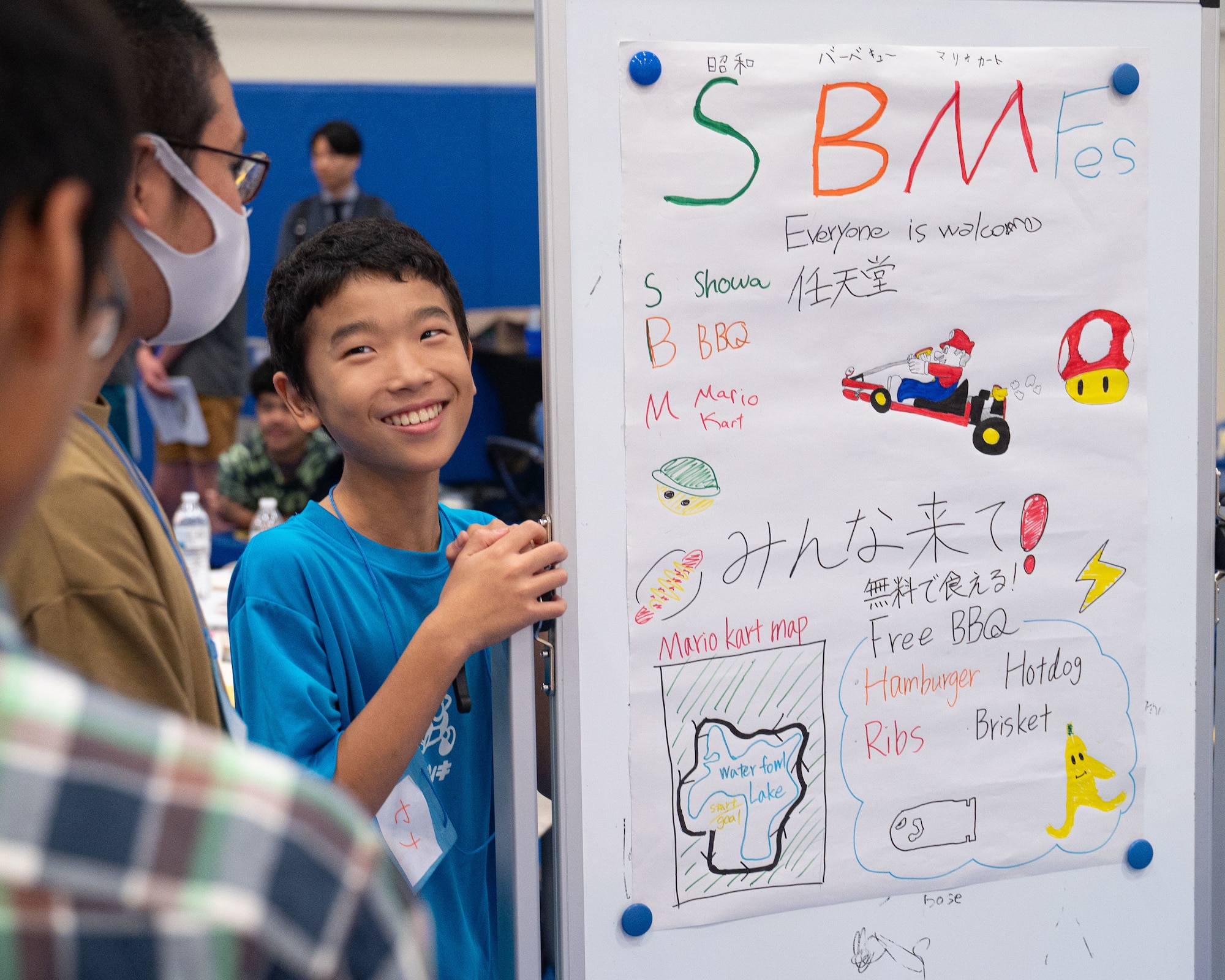 A student stands by their project and smiles at another group member.