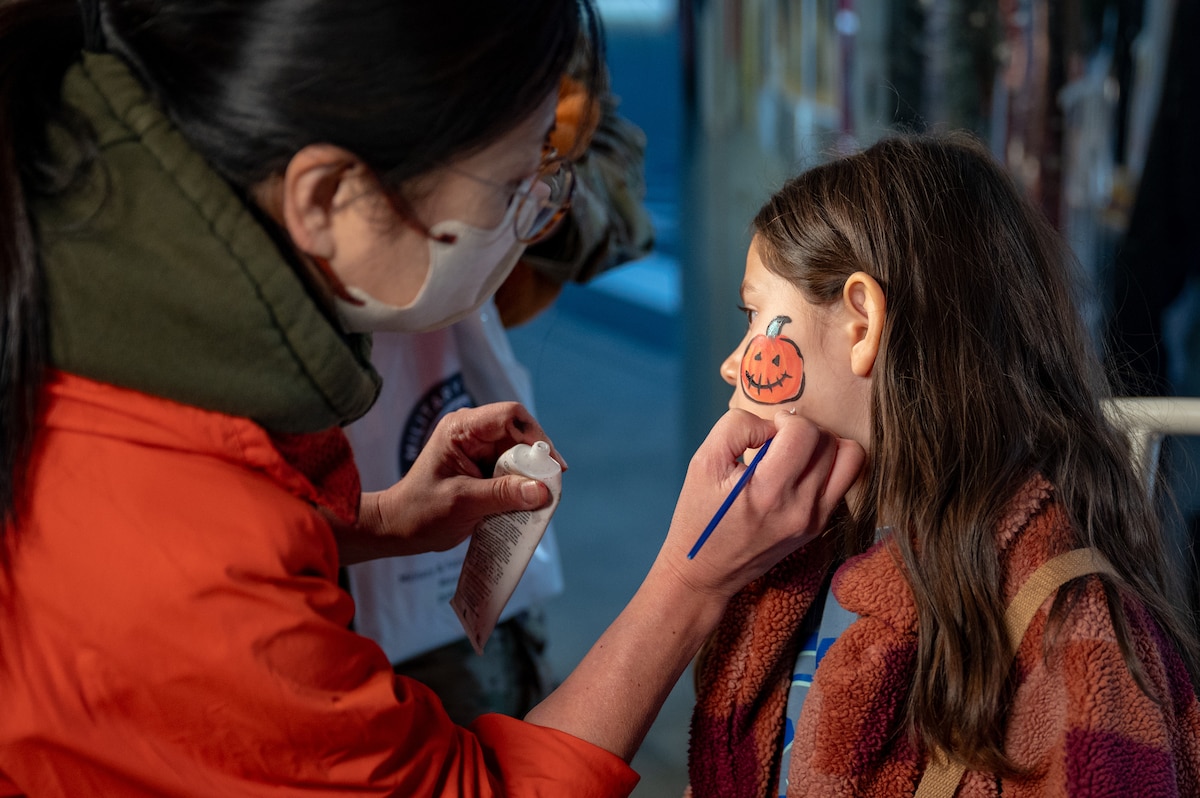 A volunteer paints a pumpkin on a participant’s face during Trunk or Treat at Misawa Air Base, Japan, Oct. 24, 2025. This celebration highlighted the 35th Fighter Wing’s focus on creating meaningful opportunities that strengthen bonds and enhance quality of life across the Misawa community. (U.S. Air Force photo by Senior Airman Brittany Russell)