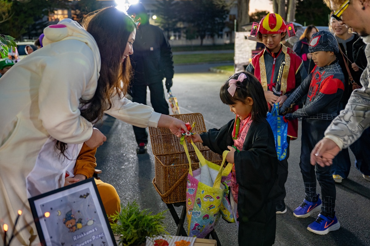 A member passes out candy to a participant during Trunk or Treat at Misawa Air Base, Japan, Oct. 24, 2025. Through events like this, the 35th Fighter Wing continues to prioritize quality experiences that promote unity, connection and community spirit. (U.S. Air Force photo by Senior Airman Brittany Russell)