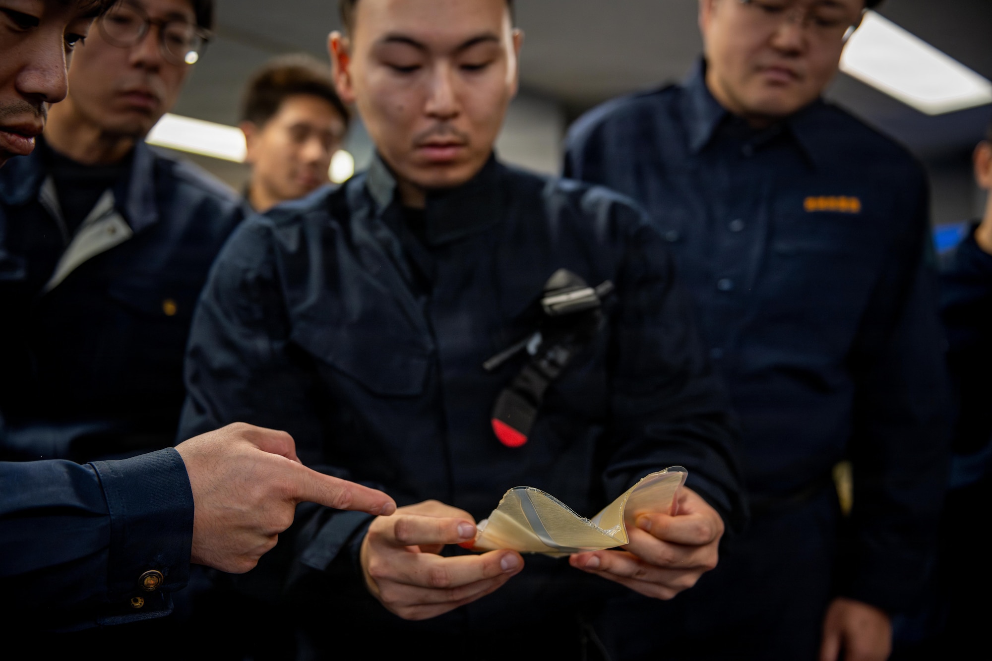 Japanese National Police Special Investigation Team members inspect a chest seal medical tool as part of a tactical combat casualty care session during a joint special weapons and tactics training event.