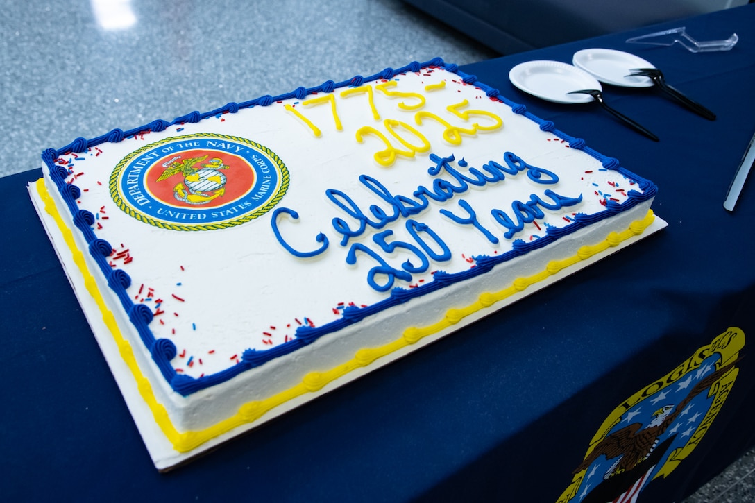 A sheet cake with white frosting and blue and yellow frosting around the edges has the U.S. Marine Corps logo on it and '1775-2025' written on it in yellow frosting and 'celebrating 250 years' in blue frosting.