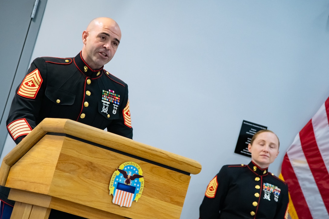 A man wearing a military uniform stands behind a lectern speaking.