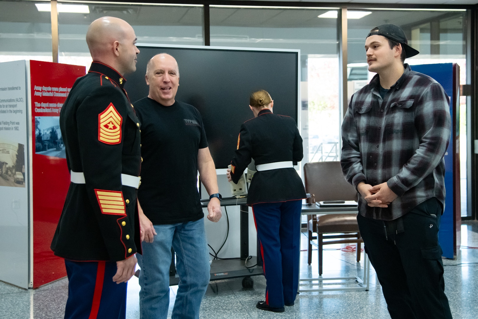 Three men stand inside of a building lobby speaking to each other, one is wearing a military uniform.