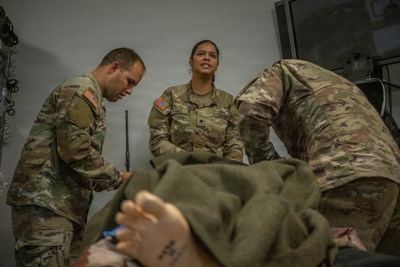 A group of soldiers provide simulated medical care to a mannequin.