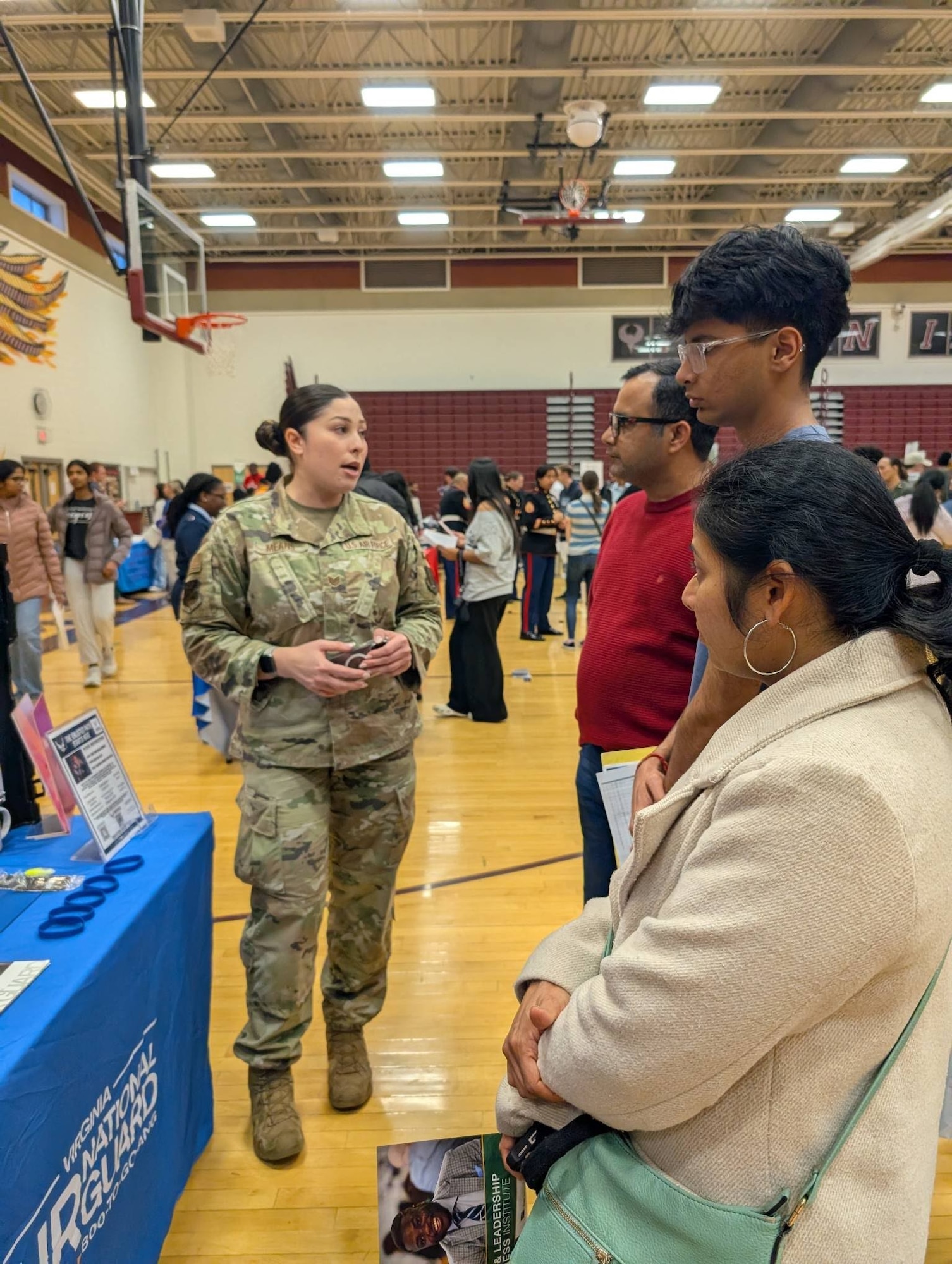 Tech. Sgt. Raychelle Means, left, speaks with students and parents in front of the Virginia Air National Guard recruiting booth in Rock Ridge High School's gymnasium in Ashburn, Virginia.