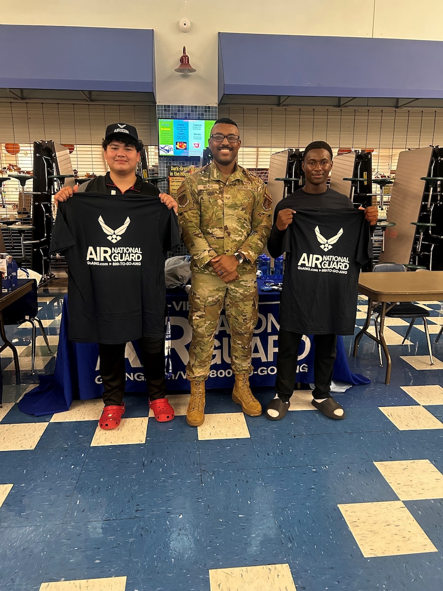 Staff Sgt. Lorenzo Walker, center, poses for a photo with two high school students in front of a Virginia Air National Guard recruiting booth.