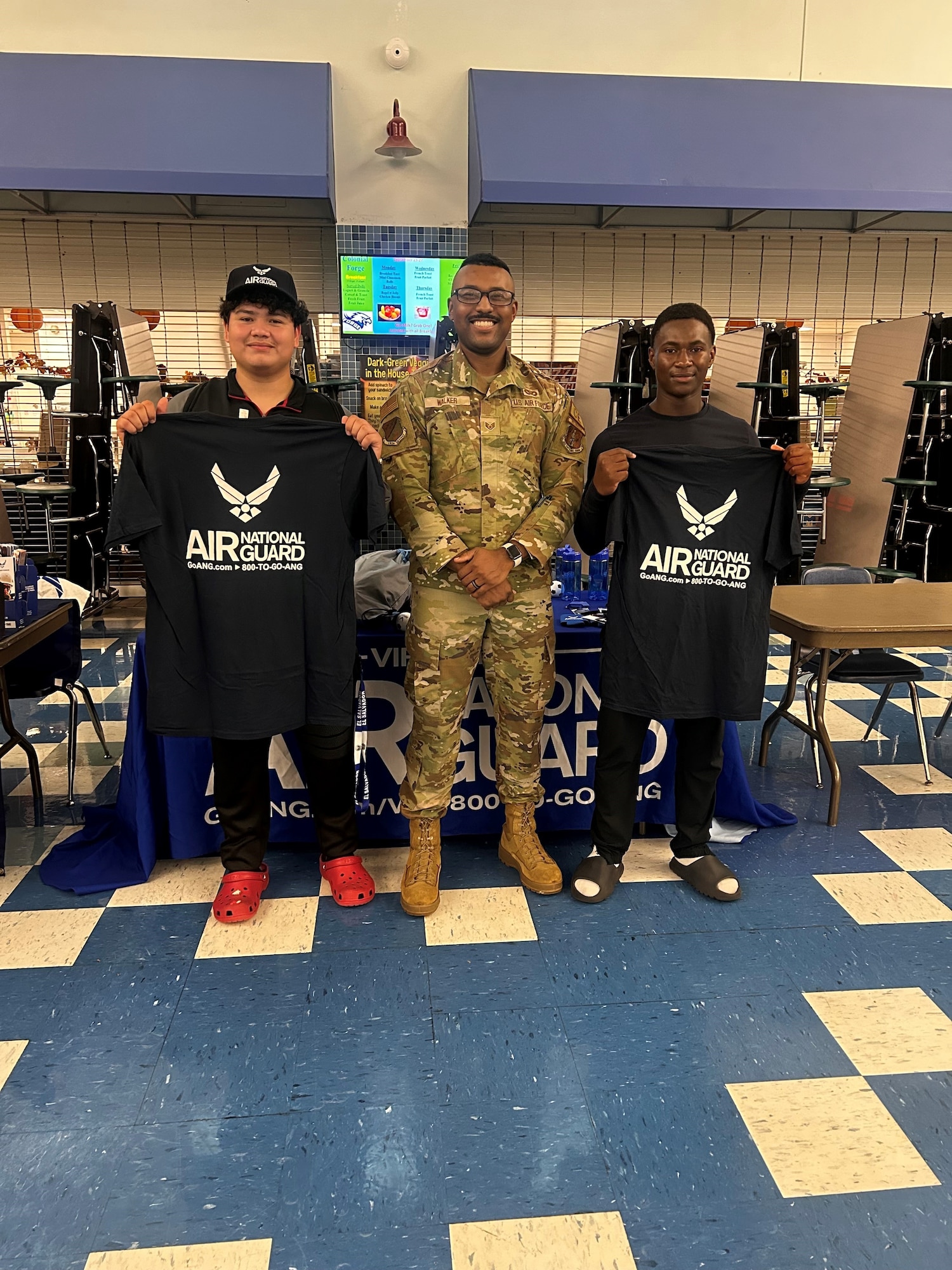 Staff Sgt. Lorenzo Walker, center, poses for a photo with two high school students in front of a Virginia Air National Guard recruiting booth.