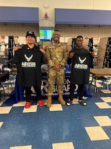 Staff Sgt. Lorenzo Walker, center, poses for a photo with two high school students in front of a Virginia Air National Guard recruiting booth.