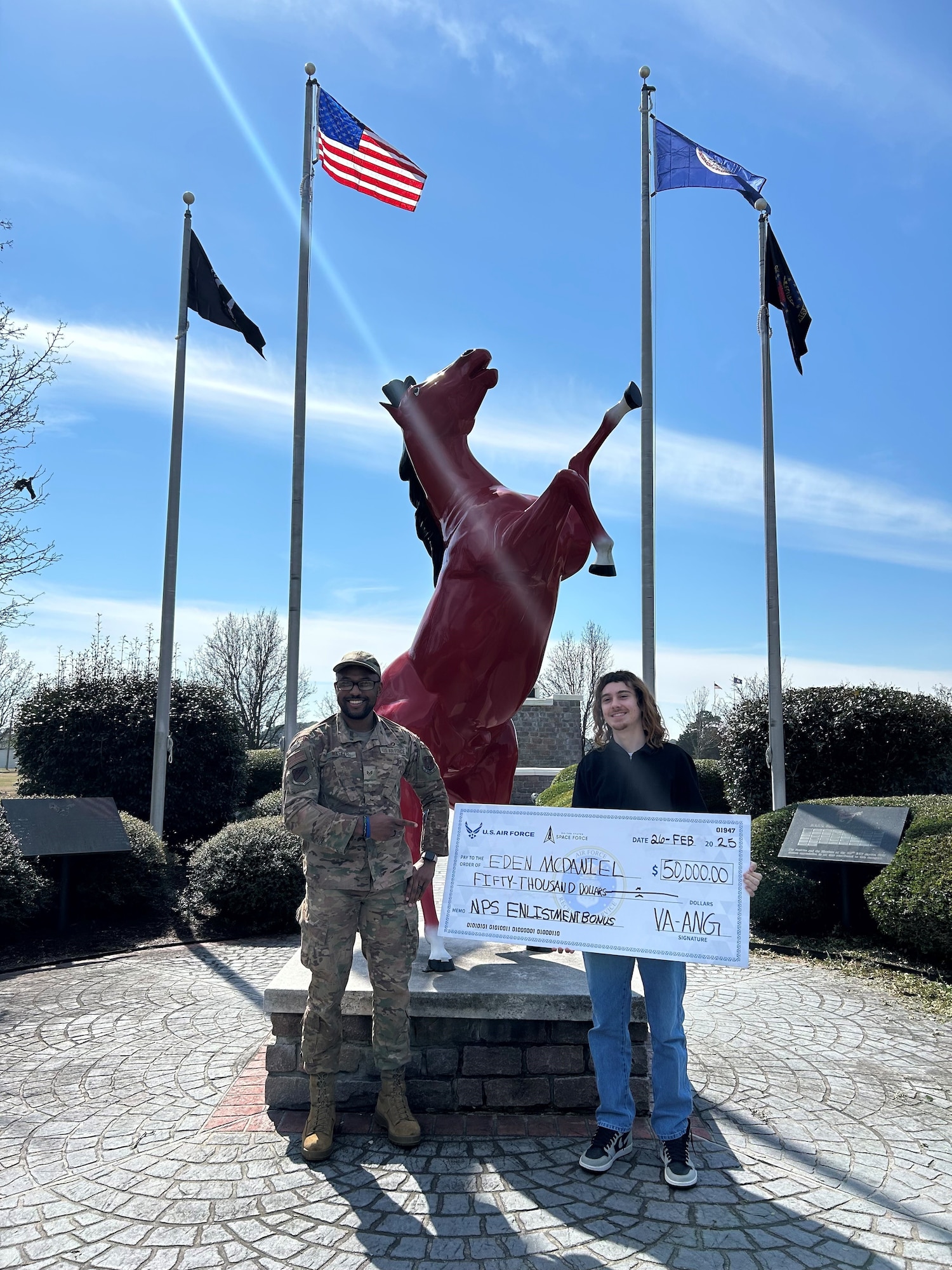 Staff Sgt. Lorenzo Walker, left, presents a signing bonus check to a new Virginia Air National Guard recruit in front of the 203rd RED HORSE statue.