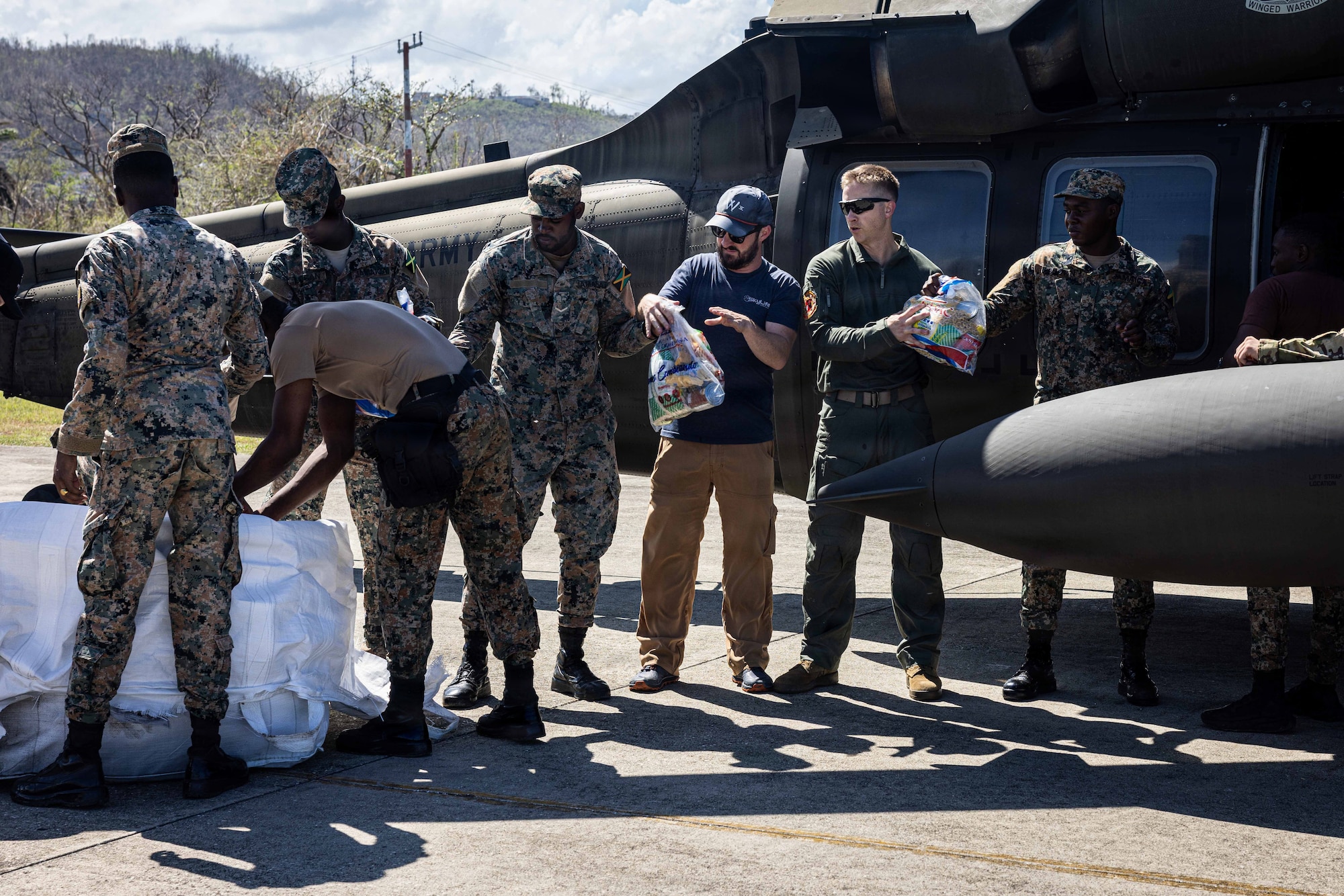Military people and civilians pass supplies in front of a helicopter