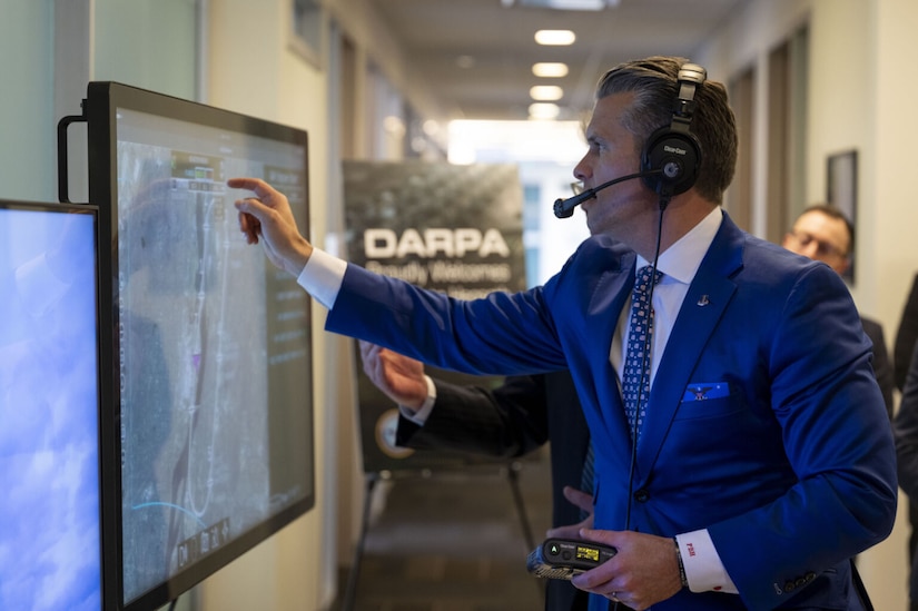 A man in business attire wears a headset and touches a television screen.