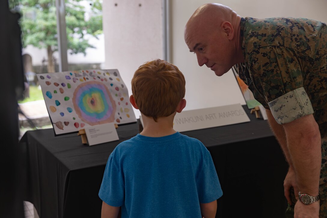 A student from the Matthew C. Perry Primary School describes his artwork to U.S. Marine Corps Col. Kenneth Rossman, the commanding officer of Marine Corps Air Station Iwakuni, and a native of Pittsburgh, Pennsylvania, during the September art awards presentation at MCAS Iwakuni, Japan, Sept. 25, 2025. The air station presented awards for its monthly art competition in which students attending schools at the air station showcase their artistic talent through different art mediums. (U.S. Marine Corps photo by Lance Cpl. Ella Cadby)
