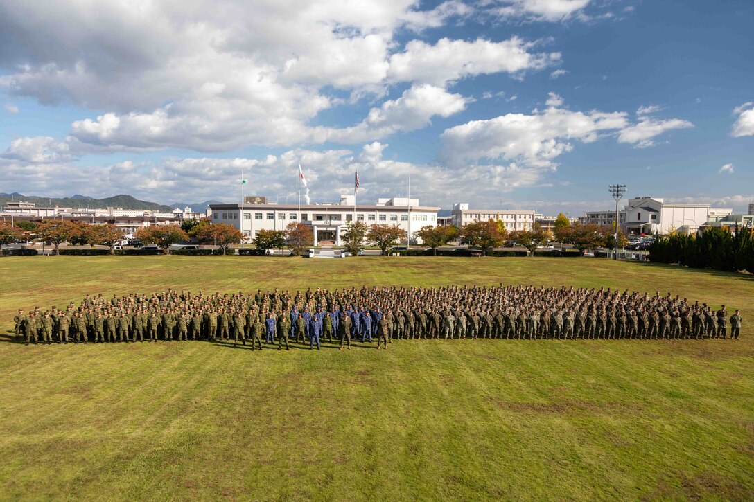 U.S. Marines and Sailors with Headquarters and Headquarters Squadron (HHS), Marine Corps Air Station Iwakuni, Japan Ground Self-Defense Force members with 13th Brigade, Middle army, and Japan Maritime Self-Defense Force members with Fleet Air Wing 31, pose for a group photo during the closing ceremony for exercise Active Shield 26 at MCAS Iwakuni, Japan, Oct. 28, 2025. Active Shield is an annual bilateral exercise hosted by MCAS Iwakuni that strengthens interoperability between U.S. and Japanese forces and enhances the defense capability of USINDOPACOM. (U.S. Marine Corps photo illustration by Lance Cpl. Rylan Adcock)