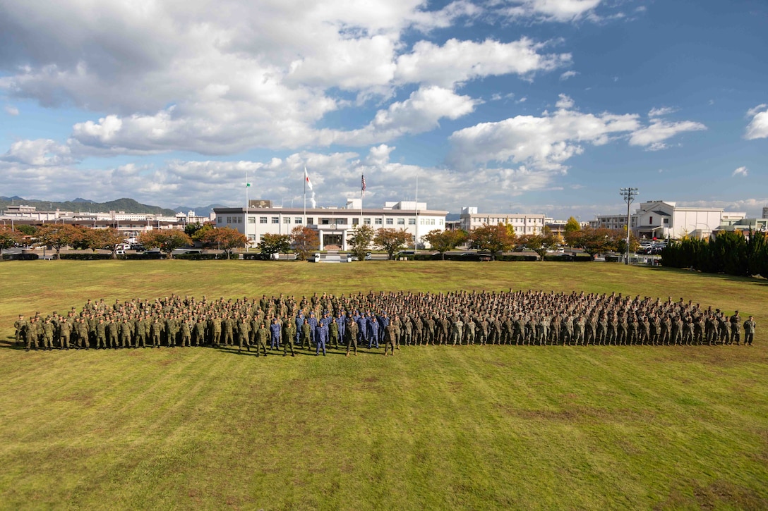 U.S. Marines and Sailors with Headquarters and Headquarters Squadron (HHS), Marine Corps Air Station Iwakuni, Japan Ground Self-Defense Force members with 13th Brigade, Middle army, and Japan Maritime Self-Defense Force members with Fleet Air Wing 31, pose for a group photo during the closing ceremony for exercise Active Shield 26 at MCAS Iwakuni, Japan, Oct. 28, 2025. Active Shield is an annual bilateral exercise hosted by MCAS Iwakuni that strengthens interoperability between U.S. and Japanese forces and enhances the defense capability of USINDOPACOM. (U.S. Marine Corps photo illustration by Lance Cpl. Rylan Adcock)