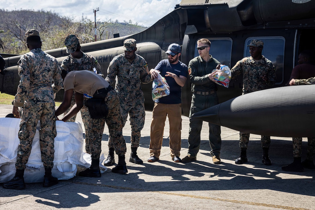Military people and civilians pass supplies in front of a helicopter