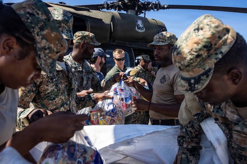 Several men in camouflage military uniforms move bags of food into a helicopter.