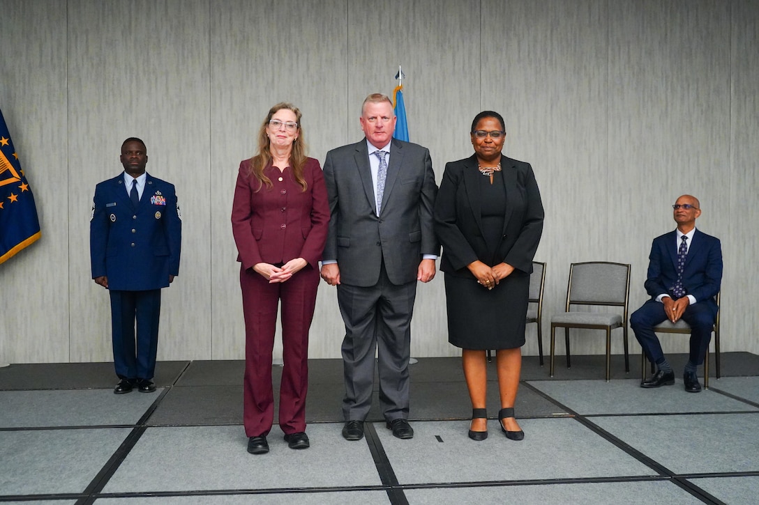 Two women and one man stand at the center of the floor near flags