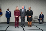 Two women and one man stand at the center of the floor near flags