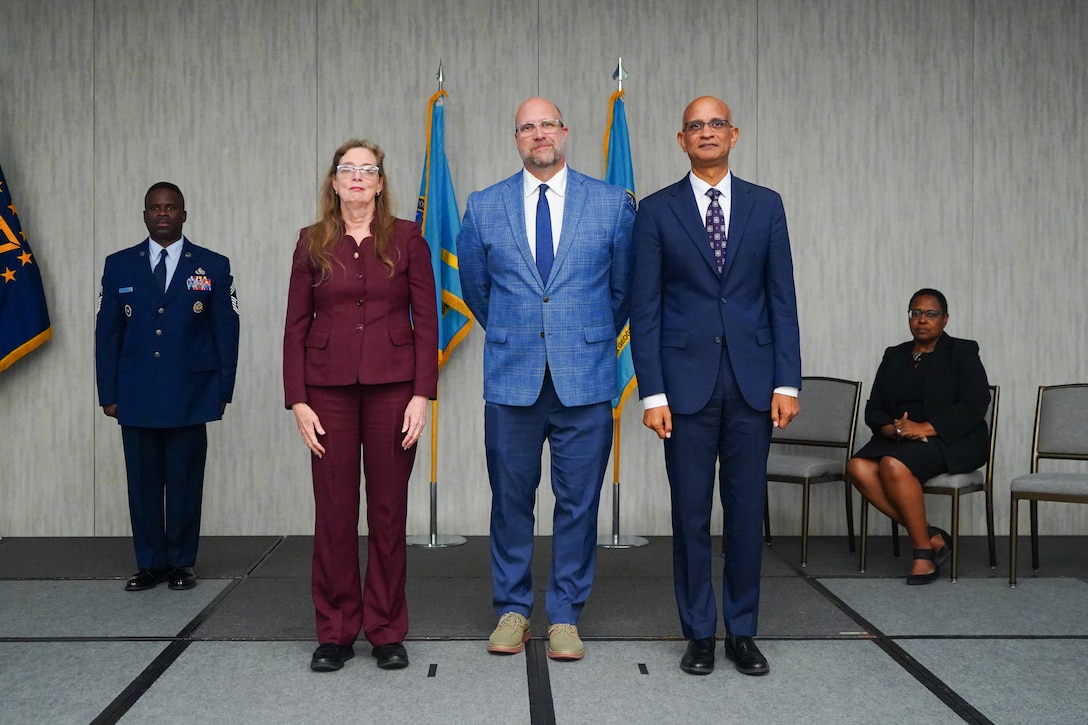 A woman and two men stand near flags