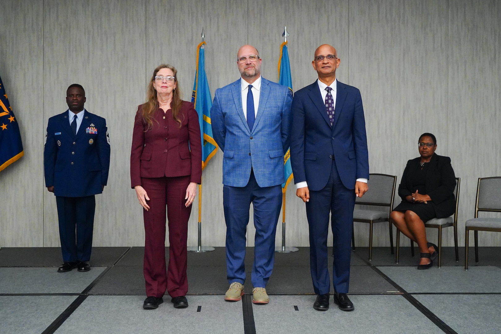 A woman and two men stand near flags