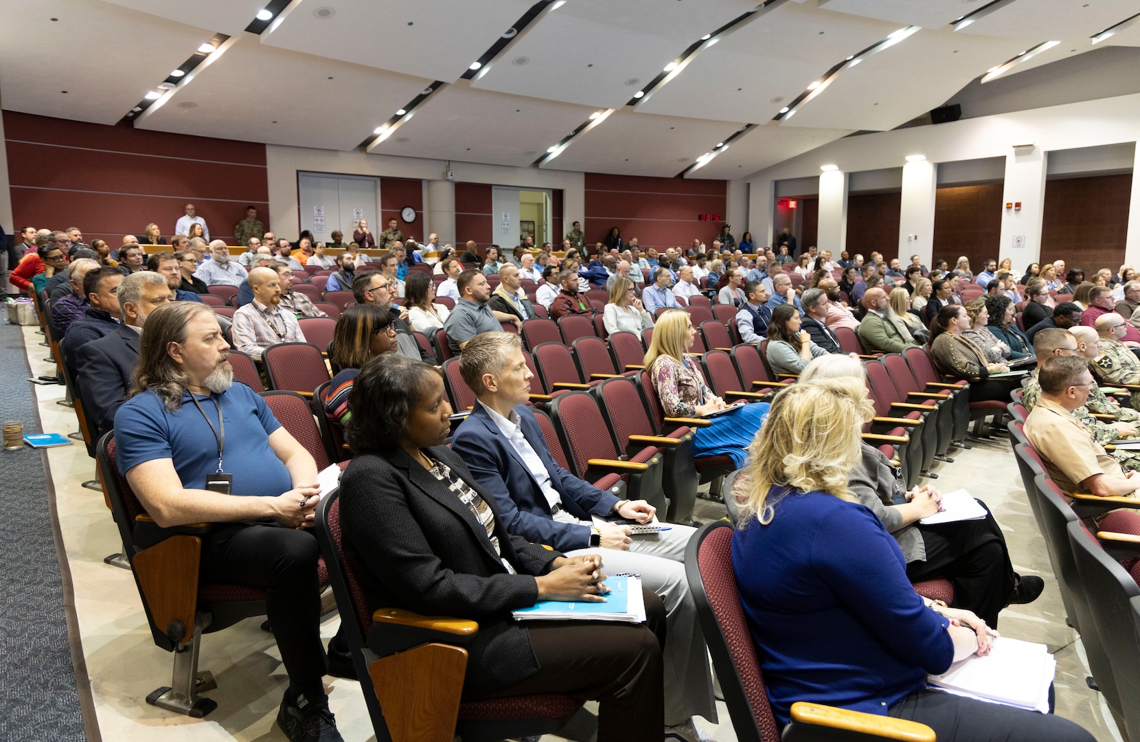 A large group of people are seated in a auditorium with two tones of soft red and pink colors.