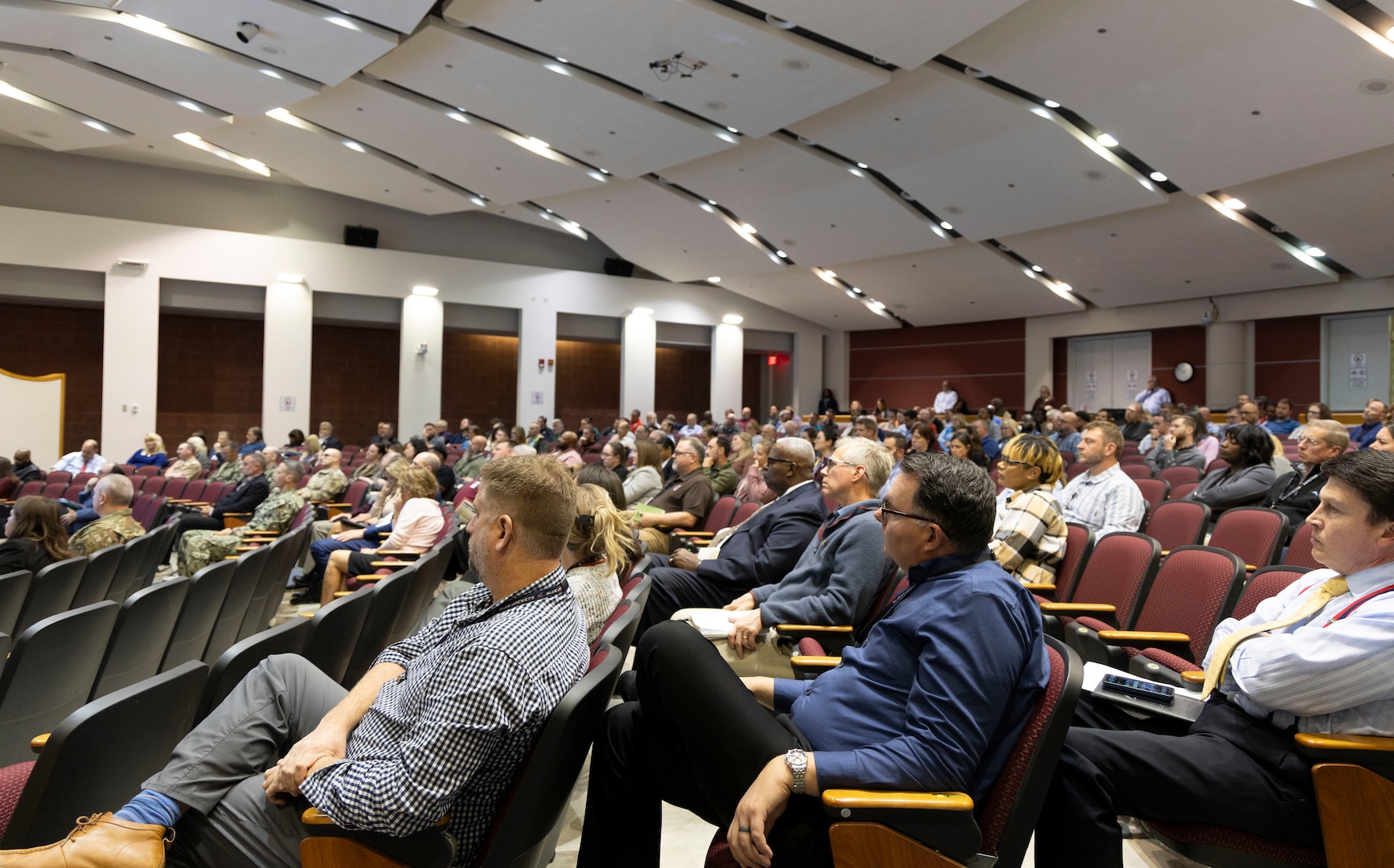 A large group of people sit in a auditorium with pink and red tones.