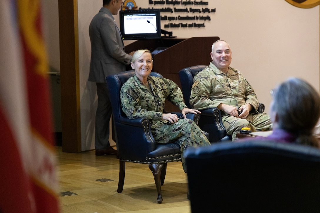 A man and a woman smile on stage. Both are in uniform.