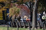 Soldiers walk down the street surrounded by fall trees. Both are wearing sunglasses with hand tucked behind their chest protective gear.