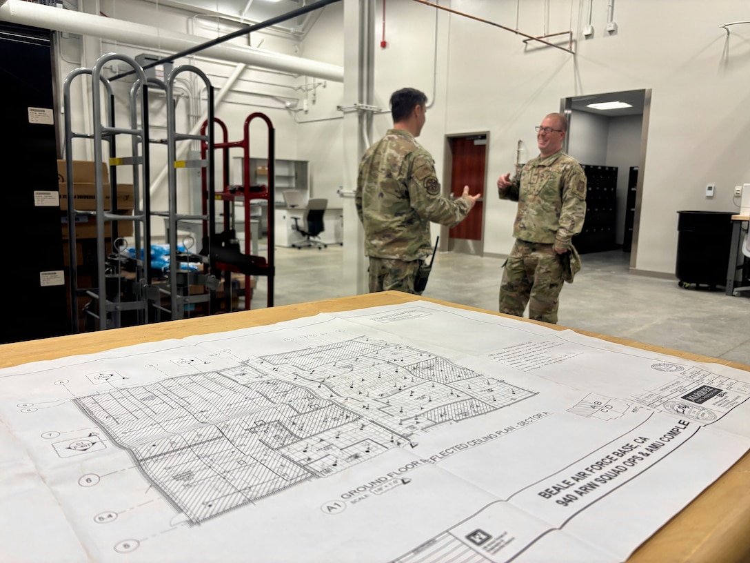 Two airmen talk inside a hangar as blueprints of the new Squadron Operations and Aircraft Maintenance Unit facility sit nearby at Beale Air Force Base, California on Nov. 14, 2025.