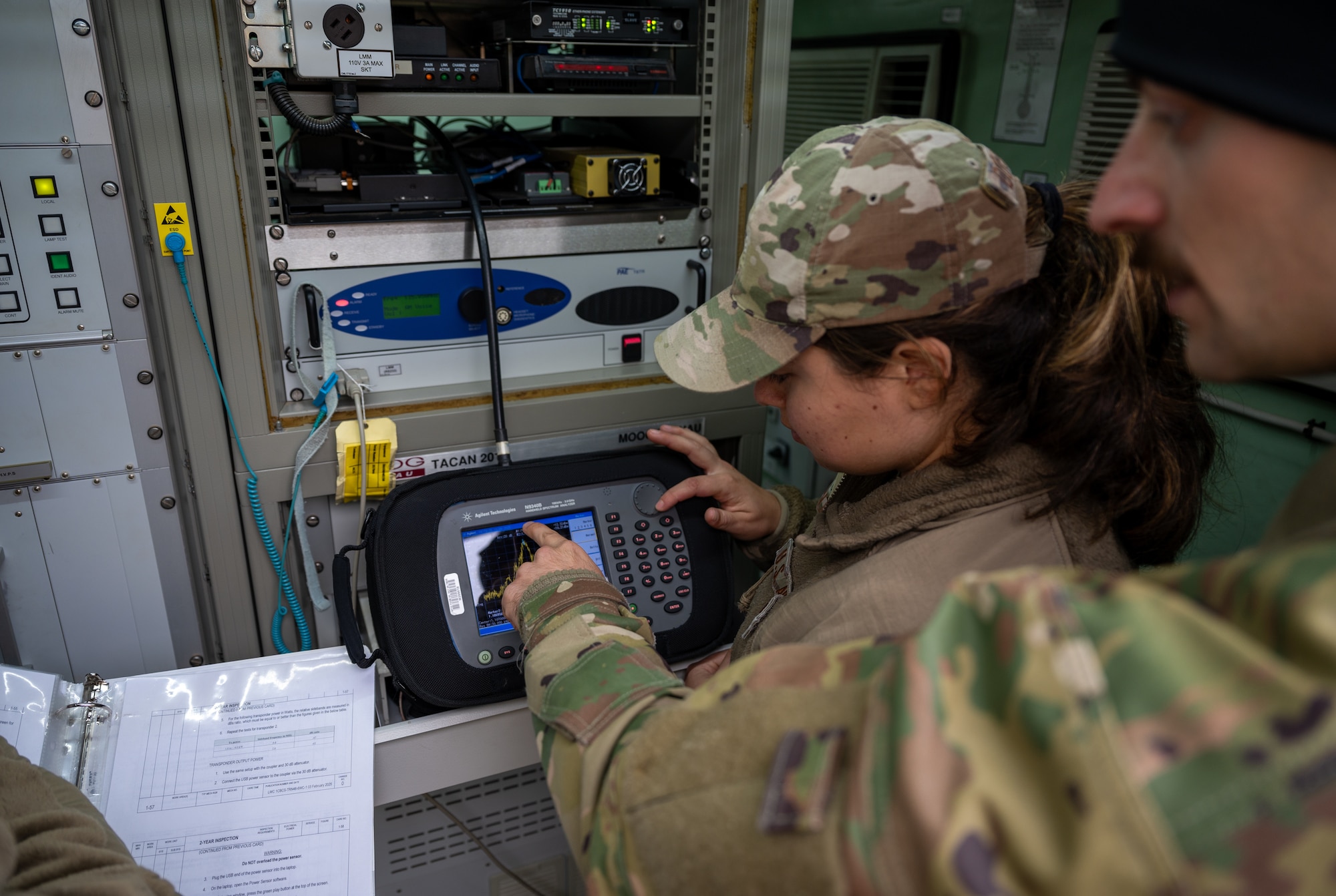 U.S. Air Force Staff Sgt. Casey Dorantes, 2nd Combat Weather Systems Squadron radar airfield weather system technician, and Staff Sgt. Chad Swanson, 1st Combat Communications Squadron noncommissioned officer in charge of tactical air field training, analyze the spectrum output of a TRN-48 Tactical Air Navigation System at Ramstein Air Base, Germany, Oct. 9, 2025. The TACAN system helps pilots to pinpoint their position and distance from an airfield even in austere conditions. (U.S. Air Force photo by Senior Airman Jared Lovett)