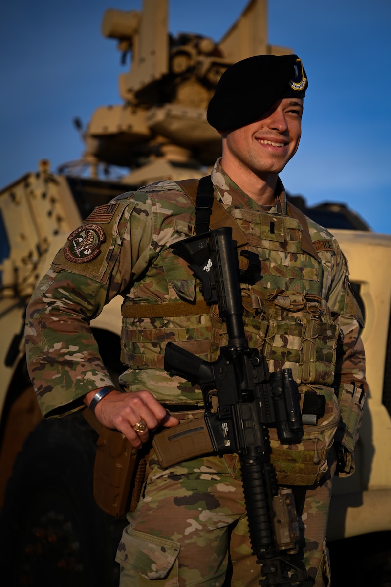 a security forces airmen leaning up against a combat vehicle smiling and laughing, beret on and gun across their chest, golden sunlight lighting