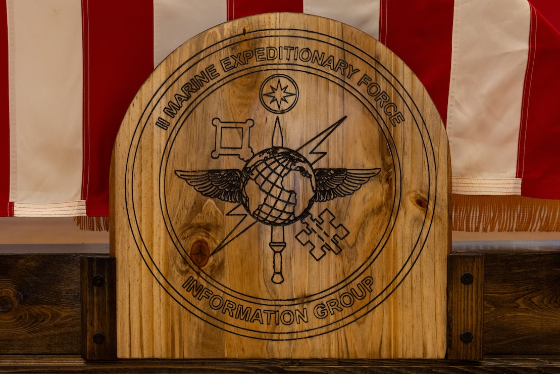 The new insignia for the II Marine Expeditionary Force Information Group displayed front and center during the ceremony on U.S. Marine Corps Base Camp Lejeune, North Caroline, Oct. 6, 2025. The revealing of the new insignia represents the many elements and fundamentals that celebrated the remarkable progress made over the recent, past, and advancing mission. (U.S. Marine Corps photo by Lance Cpl. Allison White)