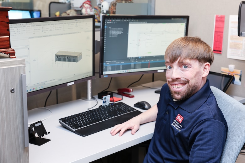 Man sits at desk with two monitors and keyboard.