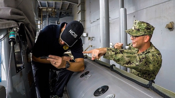 NCIS Special Agent holding a flashlight while Navy Chief Petty Officer points