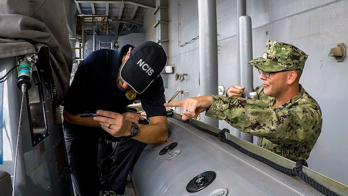 NCIS Special Agent holding a flashlight while Navy Chief Petty Officer points