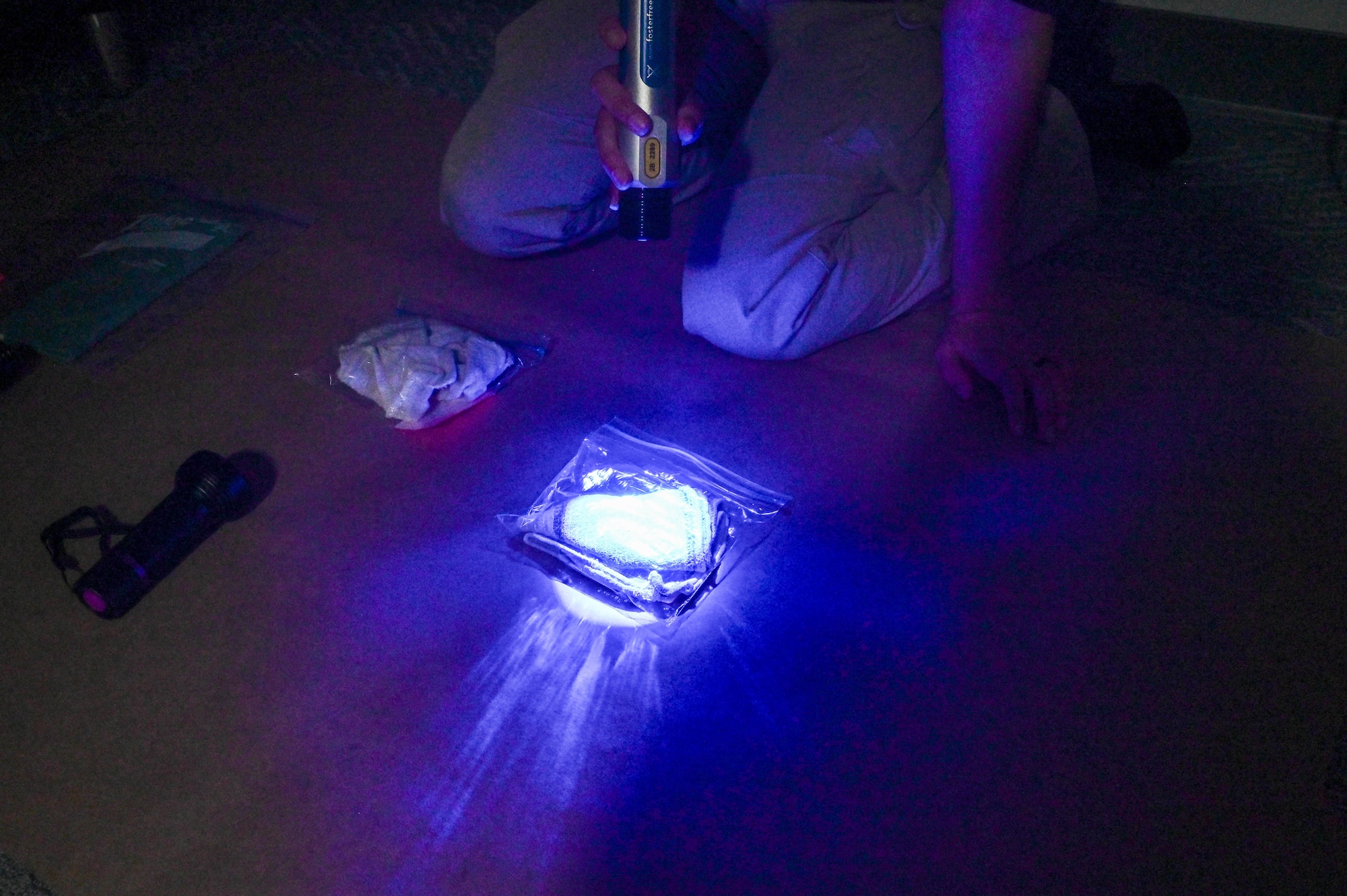 A plastic bag with a cloth inside glows blue under a forensic flashlight.