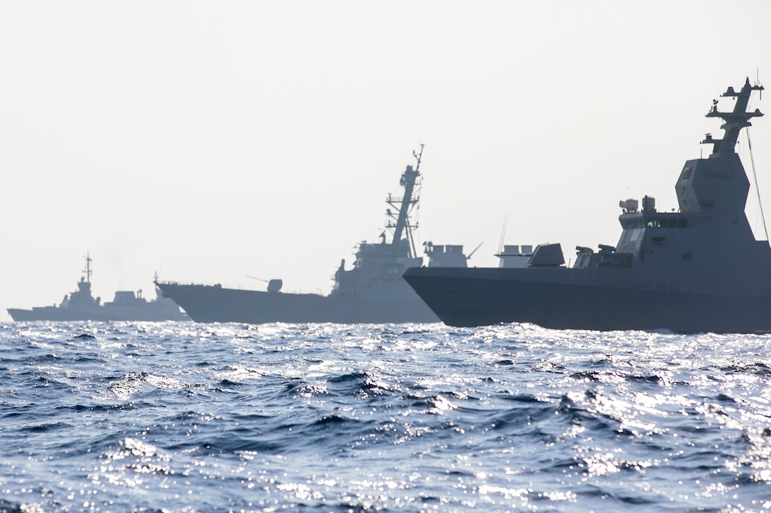 Three ships transit a choppy body of water during daytime under a hazy sky.