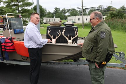 Two men stand next to a boat with duck hunting targets and animal skulls on it.