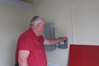 A man in a red shirt turns off a power box.