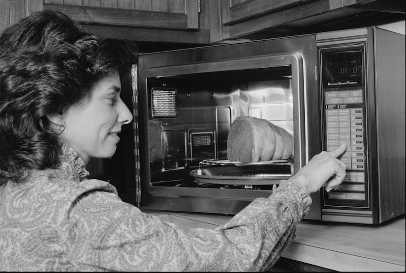 A woman presses a button on a microwave that holds a large piece of meat.